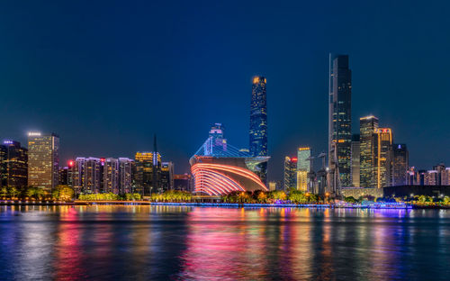 Illuminated buildings by river against sky in city at night