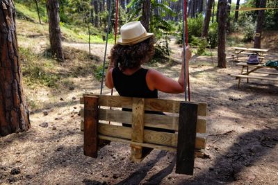 Rear view of woman sitting on swing in forest