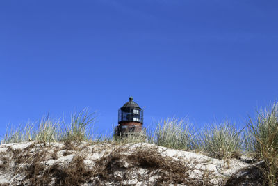 Lighthouse amidst buildings against clear blue sky