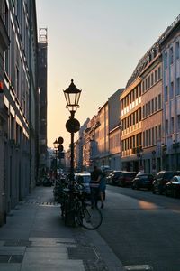 Street light on sidewalk by road amidst buildings in city during sunset