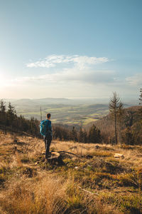 Enthusiastic traveller stands on a stump in a clear-cut forest, looking down into the valley