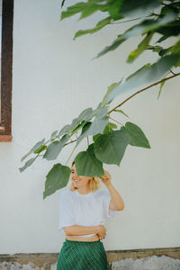 Woman holding plant against wall
