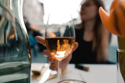 Close-up of wineglass on table against woman at restaurant