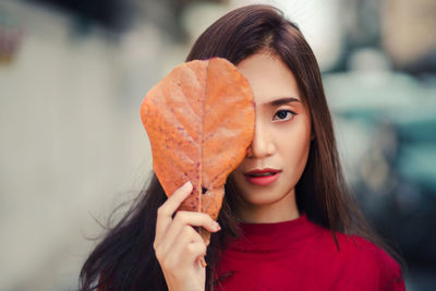 Portrait of young woman holding leaf outdoors