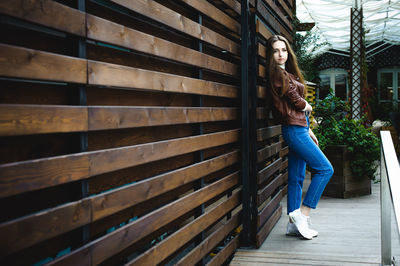 Portrait of beautiful young woman leaning on wooden wall