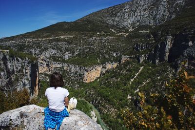 Rear view of woman standing on cliff against mountains