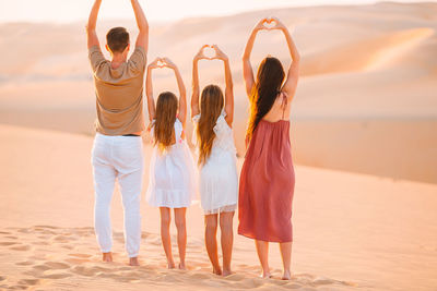 Rear view of women standing at beach during sunset