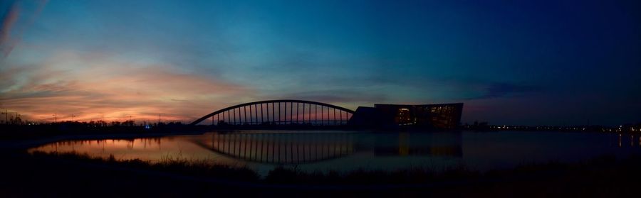 Silhouette bridge over river against sky at sunset