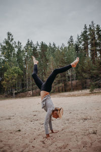 Full length of girl doing handstand at beach against trees