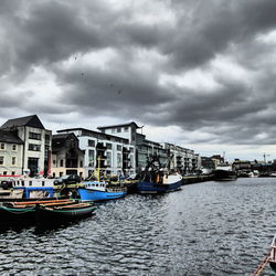 Boats moored in river by buildings against sky