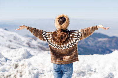 Rear view of woman standing with arms outstretched on snow against sky