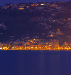 High angle view of illuminated buildings by sea against sky at night