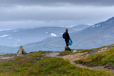Side view of senior woman standing on mountain against cloudy sky