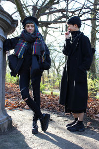 Friends standing against bare trees at park