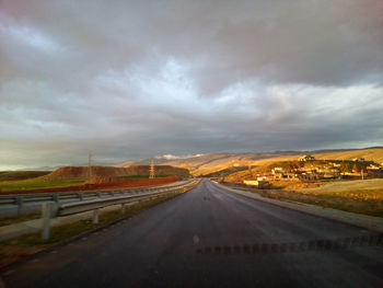 Road passing through landscape against dramatic sky