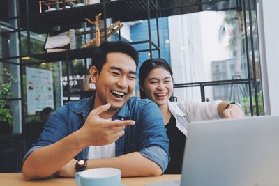 Smiling young woman using phone while sitting on table