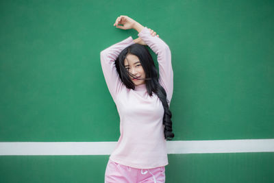 Portrait of young woman with arms raised standing against yard line in court