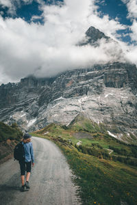 Rear view full length of female hiker walking on road against mountain