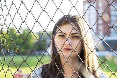 Portrait of young woman standing against chainlink fence