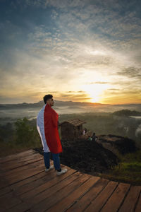Rear view of man with indonesian flag standing on wood during sunset