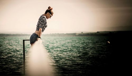 Side view of young woman in sea against sky