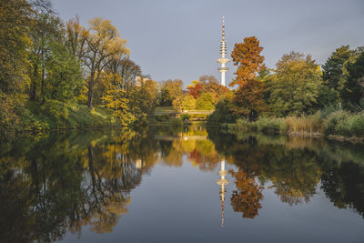 Germany, hamburg, autumn trees reflecting on surface of shiny lake in wallanlagen park