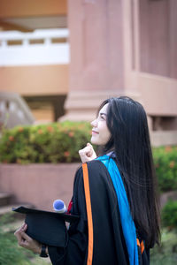 Young woman looking down while standing against built structure