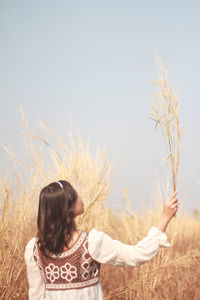 Rear view of woman with arms raised on field against sky