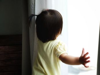 Rear view of baby girl standing by window at home