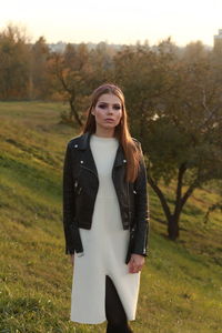 Portrait of beautiful young woman standing on field during sunset