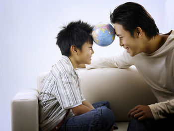 Father and son with globe sitting against wall on sofa
