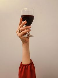 Cropped hand of woman holding wineglass against pink background