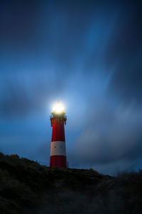 Lighthouse by building against sky at dusk
