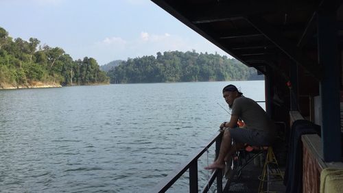 Side view of man sitting on railing against sky
