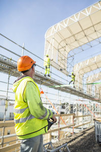 Side view of construction worker looking at colleagues working at site