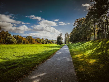 Empty road along trees and plants against sky