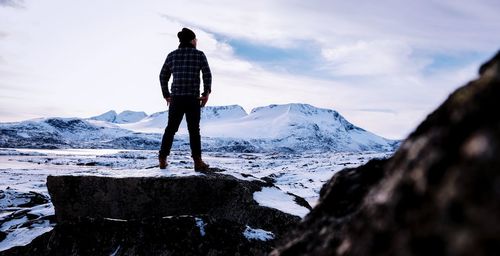 Rear view of man standing on snowcapped mountain