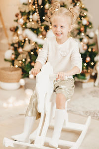 A blonde girl in a sweater rides a wooden horse at home 