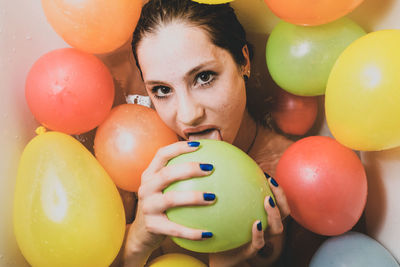 Portrait of woman licking colorful balloons at home