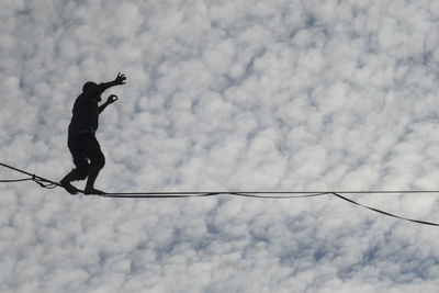 Low angle view of silhouette bird perching on cable against cloudy sky