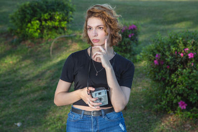 Portrait of man holding camera while standing against plants