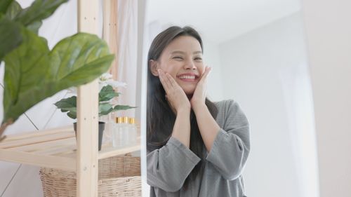 Over a spa background, a young gorgeous woman with a towel on her head cheerfully touches her.