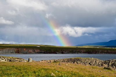 Scenic view of rainbow over field by lake against sky