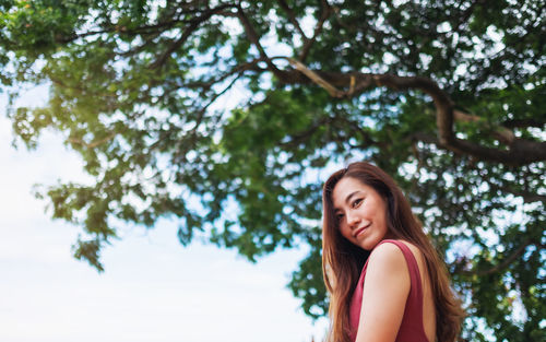 Portrait of smiling woman standing against tree