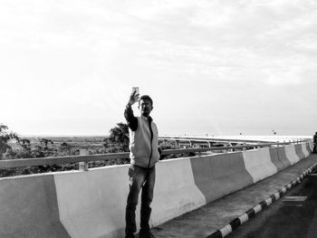 Man taking selfie while standing by retaining wall against sky