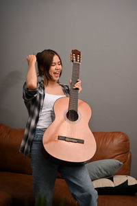 Young woman playing guitar against wall