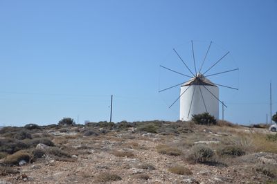 Low angle view of windmill on hill against clear blue sky
