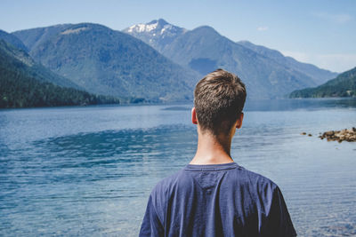Rear view of man looking at lake against mountain range