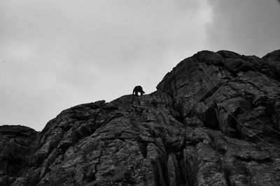 Low angle view of man climbing rock against sky