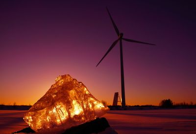 Wind turbines on land against sky during sunset